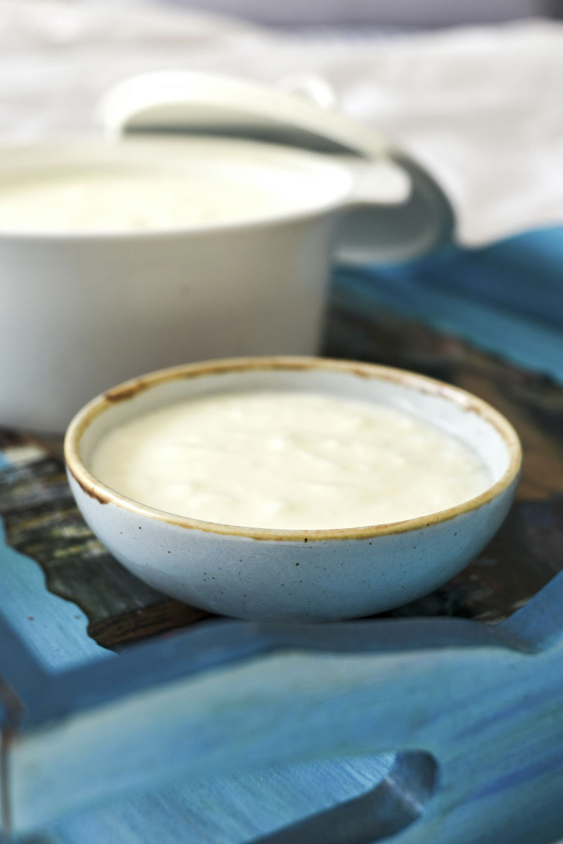 A small ceramic bowl filled with creamy white kefir, placed on a blue wooden tray with another bowl of kefir blurred in the background.